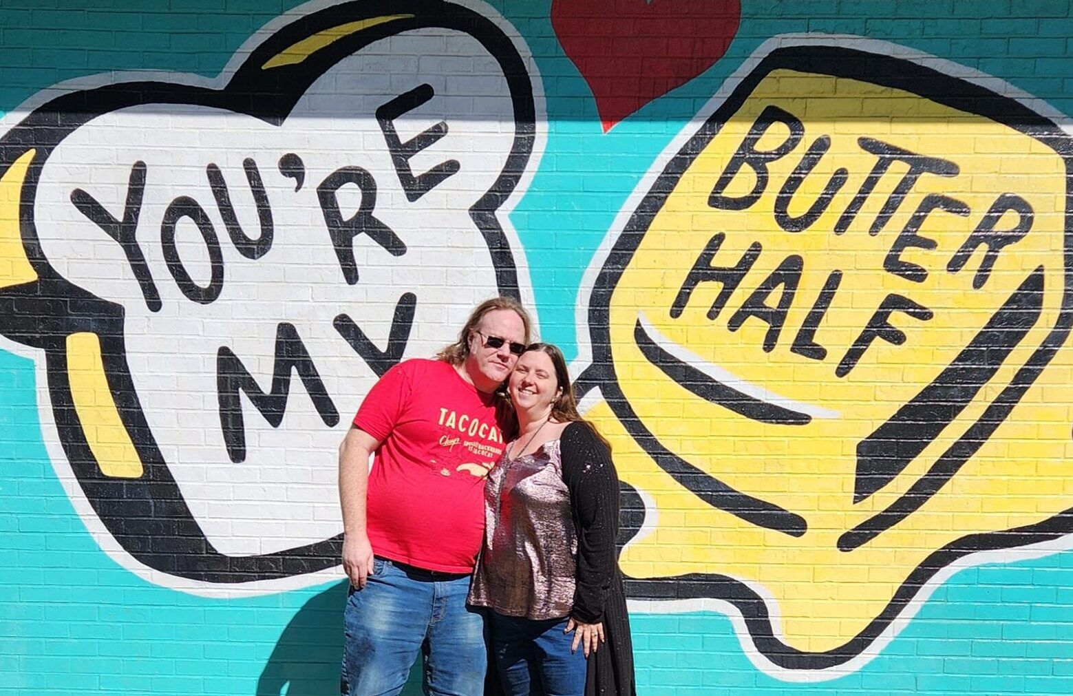 A couple standing in front of a mural that reads you are my butter half